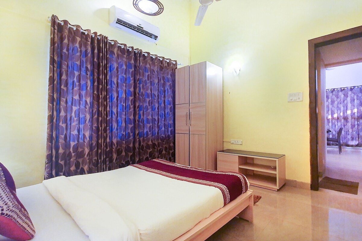 Quarto com cama, guarda-roupa, uma mesinha e porta que dá para outro cômodo.