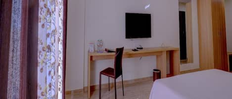 Una camera d'albergo con un letto, una scrivania con sedia, un televisore e una ventola a soffitto.