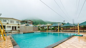 Una piscina con plataforma de madera, rodeada de edificios y un paisaje montañoso.