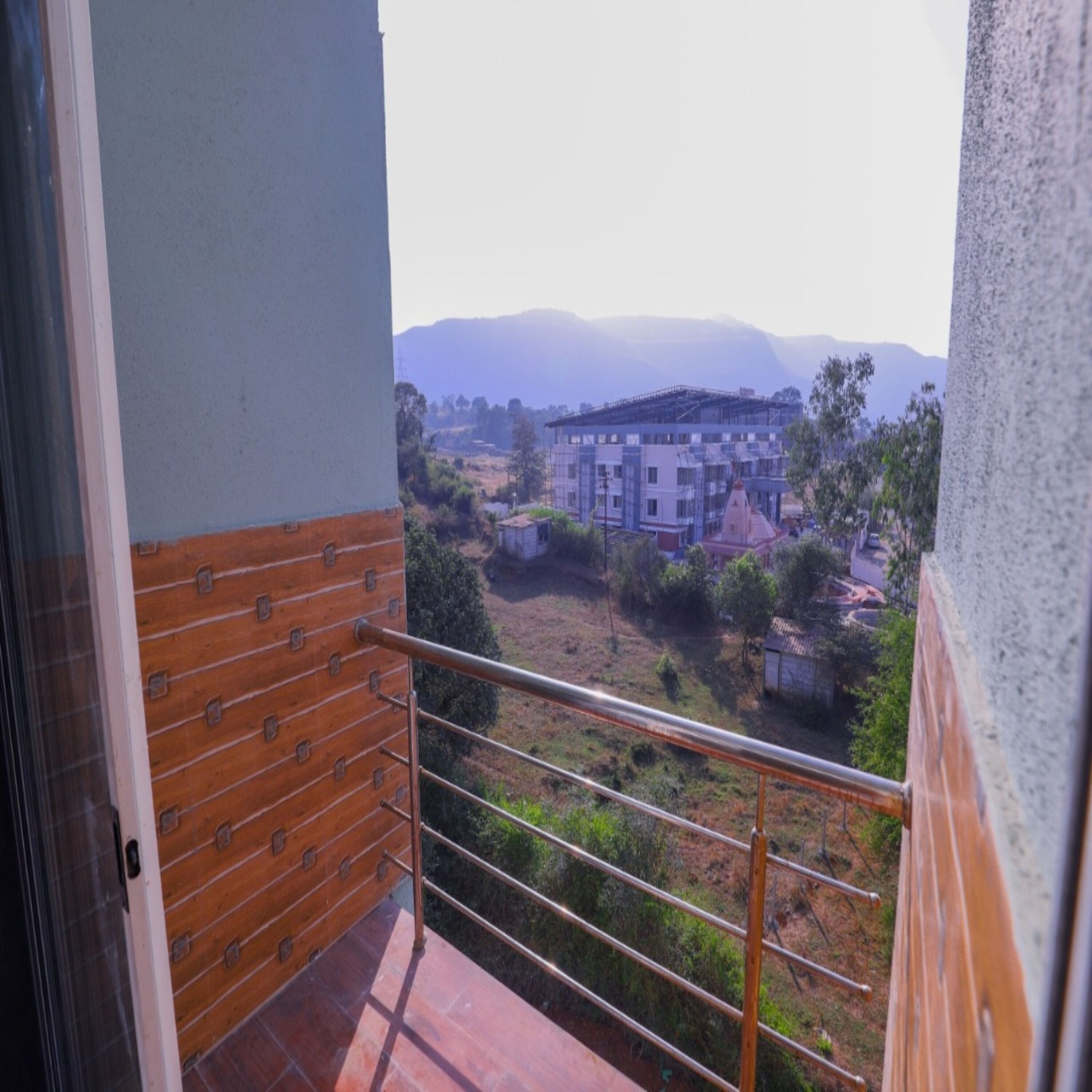 Un balcón con baranda de metal que da a una zona residencial con casas y una cadena montañosa distante.