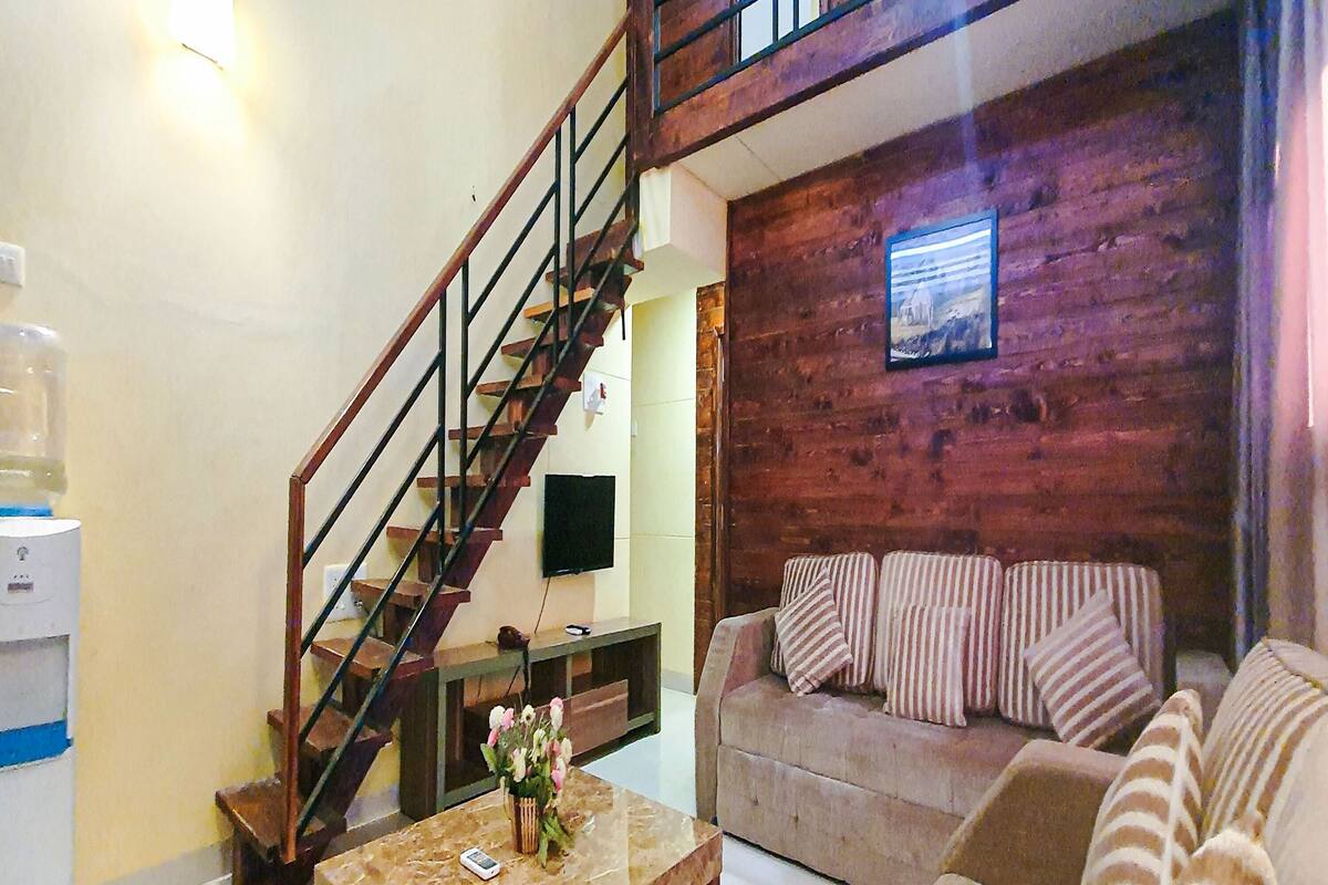 A living room with a wooden staircase, a sofa, a coffee table, and a water dispenser.