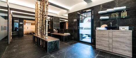 Un baño moderno con baldosas de mármol oscuro, un mueble de tocador de madera y un box de ducha de cristal.