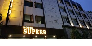 Une enseigne d’hôtel portant le nom « HÔTEL SUPERBE », illuminée par des lumières vives.
