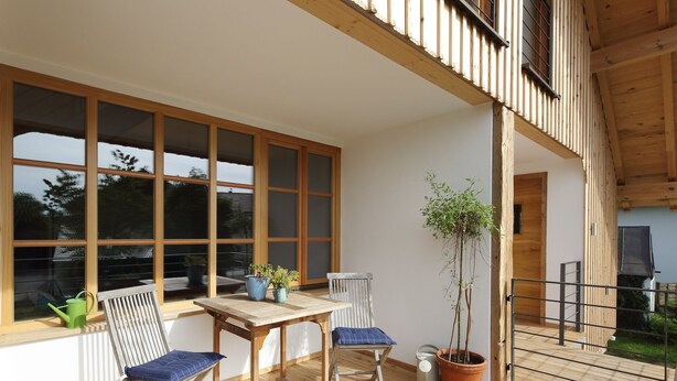 Eine Holzterrasse mit Tisch, Stühlen und Kübelpflanzen sowie großen Fenstern.