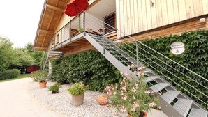 Ein hölzernes Gebäude mit einer Treppe, die zu einem Balkon führt, umgeben von Grünpflanzen und Topfpflanzen.