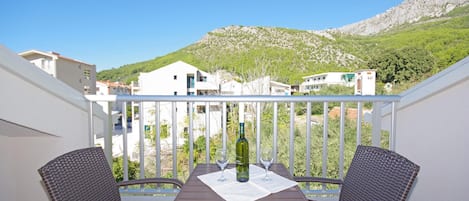 A balcony with a table and two chairs, overlooking a hillside with buildings.