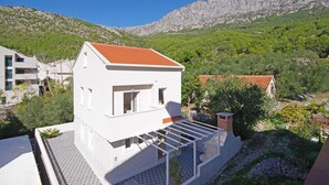 A white two-story building with a red-tiled roof, a balcony, and a view of a mountainous landscape. - Gorgeous home in Drvenik with WiFi (Drvenik)