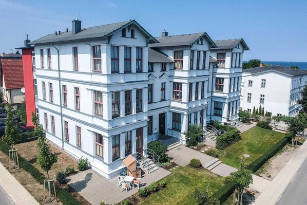 A large, white, multi-story building with a symmetrical facade, multiple windows, and a well-maintained lawn.