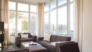 Un salon moderne avec de grandes fenêtres, un ensemble de canapés, une table basse et un téléviseur.