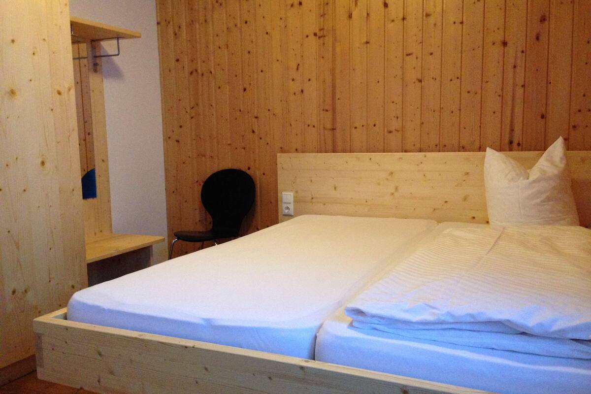 A wooden-paneled room with a bed, a chair, and a small table.