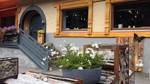 A wooden staircase leading to a door with a circular archway, a large potted plant with white flowers, and a rustic wooden bench. - Alpinhotel Zerres (Gaschurn)