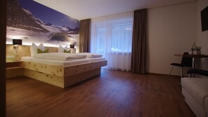 A bedroom with a wooden bed, a nightstand, a desk, a chair, and a large mural on the wall. - Alpinhotel Zerres (Gaschurn)