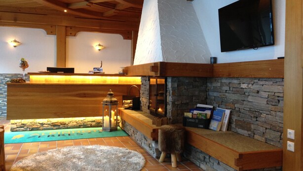 A cozy interior with a stone fireplace, wooden beams, a flat-screen TV, and a reception desk. - Alpinhotel Zerres (Gaschurn)