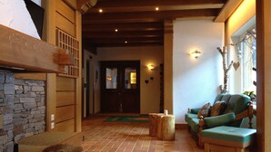 A cozy living room with a stone fireplace, wooden beams, a green sofa, and a wooden coffee table. - Alpinhotel Zerres (Gaschurn)