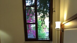 A bedroom with a bed, a window with a view of pink flowers, and a wall-mounted lamp. - Gorkem Apart Hotel (Fethiye)