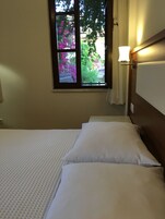 Un dormitorio con una cama, un ventanal con vistas a flores rosadas y una lámpara fijada a la pared.
