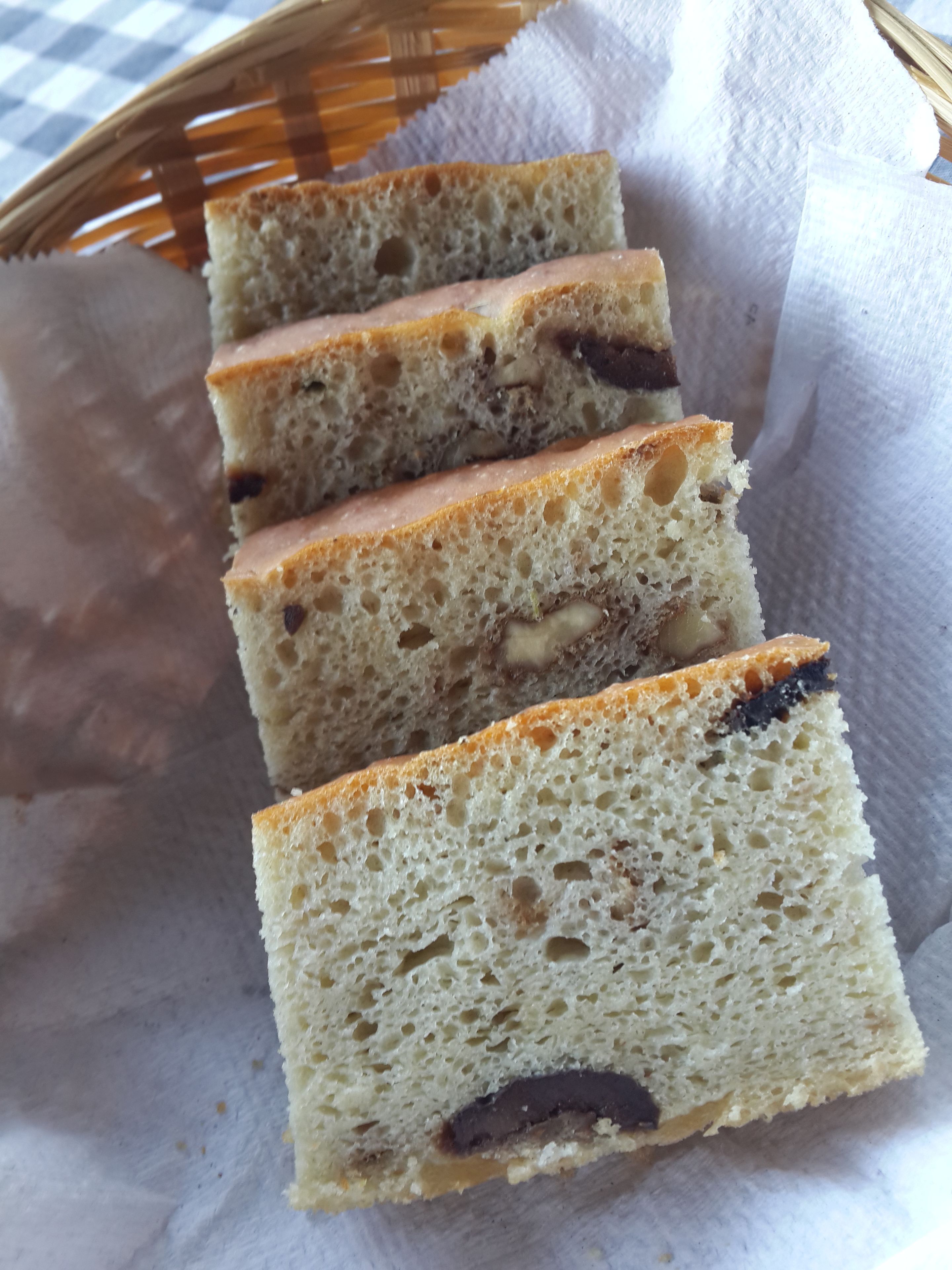 Slices of cake with visible nuts and chocolate pieces, placed on a paper towel inside a basket.