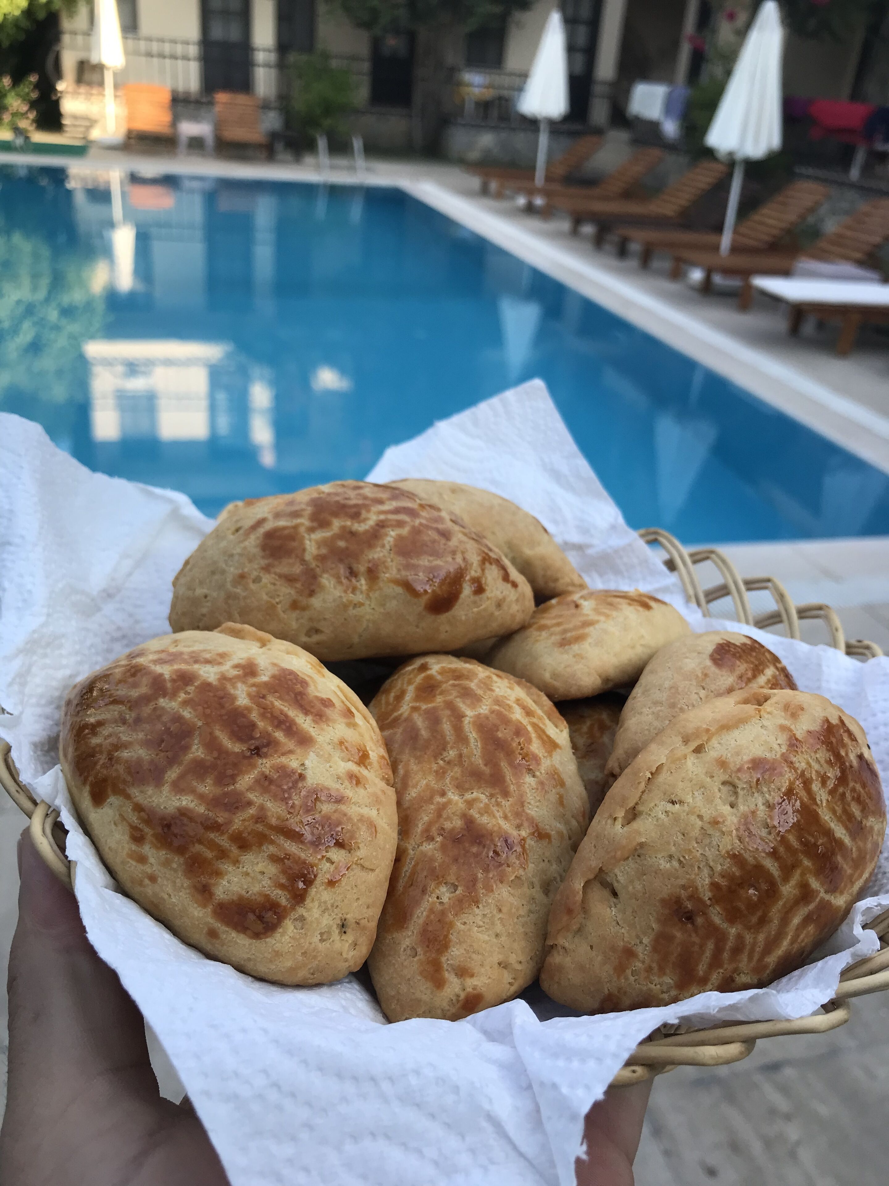 Een mand met versgebakken brood bij een zwembad, met ligbedden en parasols.