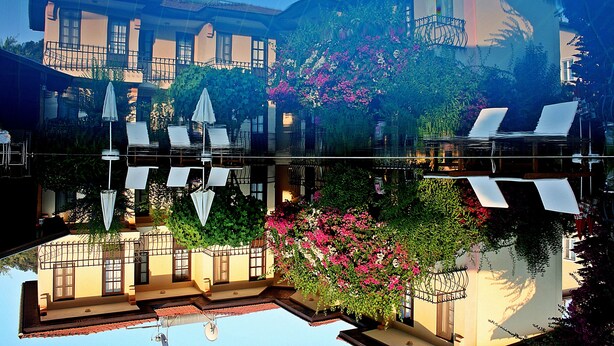 A hotel with a pool, outdoor seating, and lush greenery. - Gorkem Apart Hotel (Fethiye)