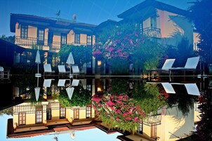 Un hotel con piscina, mobiliario exterior y abundante vegetación.