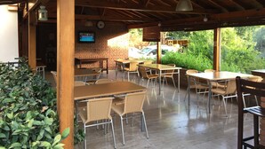 An outdoor patio with wooden tables and chairs, a brick wall, and a television screen. - Gorkem Apart Hotel (Fethiye)