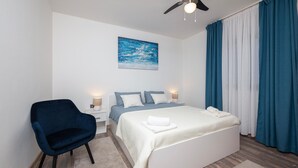 Ein Schlafzimmer mit Bett, Sessel, Nachttisch, Lampe und einem Bild an der Wand.