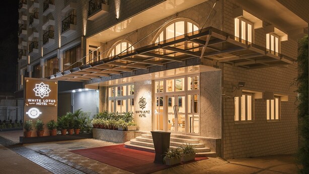 Exterior del Hotel White Lotus con una entrada destacada, alfombra roja y plantas en macetas.