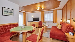 Een gezellige kamer met een eettafel, stoelen, een bank, een televisie en een houten plafond.