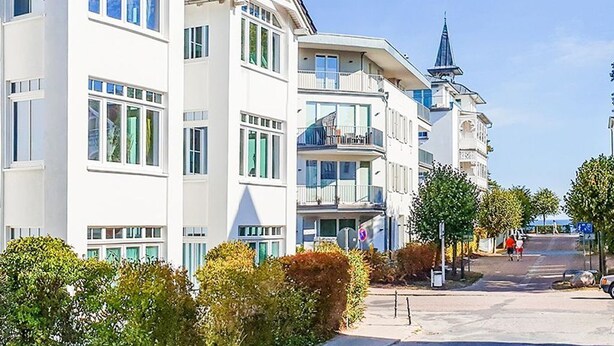 Un immeuble résidentiel à plusieurs étages, doté de balcons, avec un clocher d’église et un ciel dégagé.