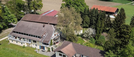 An aerial view of a large estate with multiple buildings, including a main house with a large balcony and a smaller attached structure.