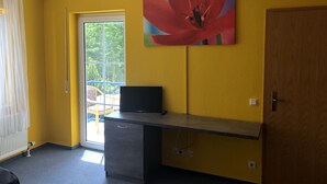 A room with yellow walls, a large window with a view of greenery, a desk with a television, and a door. - Simona Hotel Frankfurt Airport (Hofheim am Taunus)