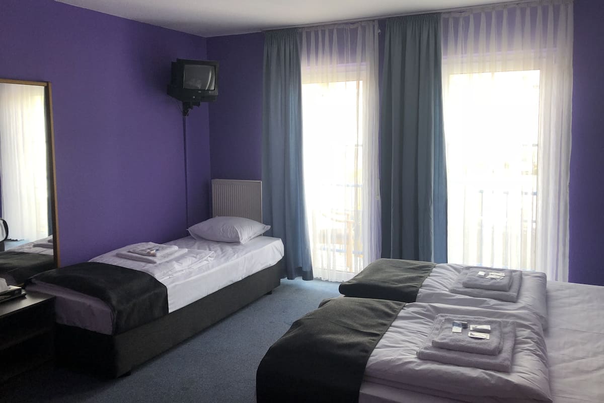 Une chambre d’hôtel avec deux lits, un téléviseur à écran plat fixé au mur et une fenêtre avec des rideaux légers.