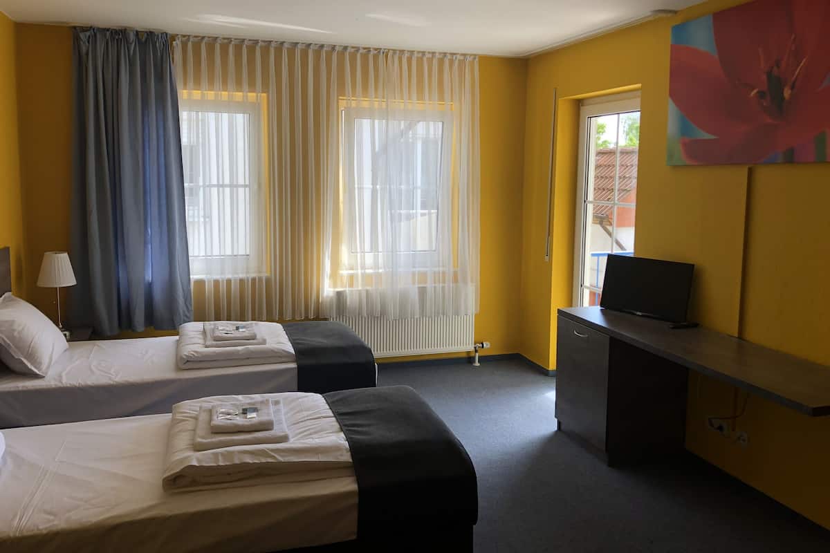 Une chambre d’hôtel avec deux lits, un bureau, une télévision et une grande fenêtre avec des rideaux.