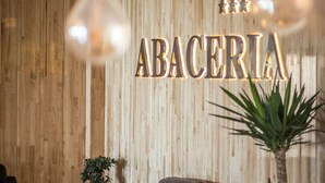 Una pared de madera con la palabra "ABACERIA" iluminada con luces, un sofá de cuero y una planta en maceta.