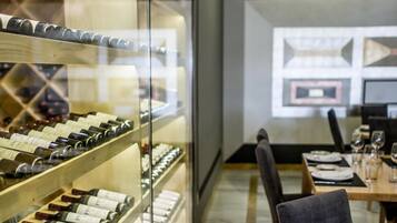 A wine cellar with shelves of wine bottles, a dining area with tables and chairs, and a modern interior design.