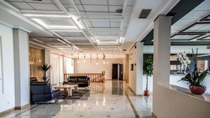 Un vestíbulo moderno con piso de mármol, asientos de cuero, iluminación colgante e hileras de plantas en macetas.