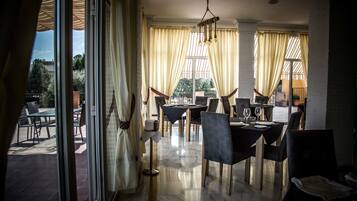 A dining area with a table set for four, a chandelier, and large windows with curtains.