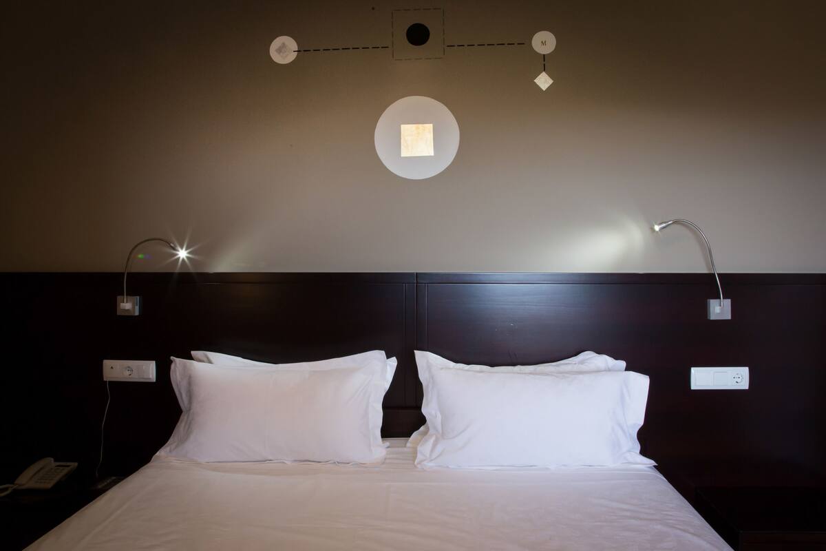 A hotel room with a large bed, two bedside lamps, a wall-mounted light fixture, and a phone on the nightstand.