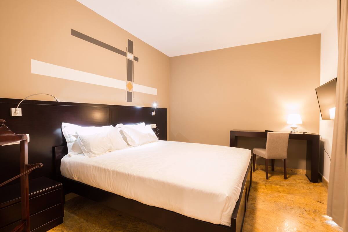 A hotel room with a large bed, a desk, and a chair.