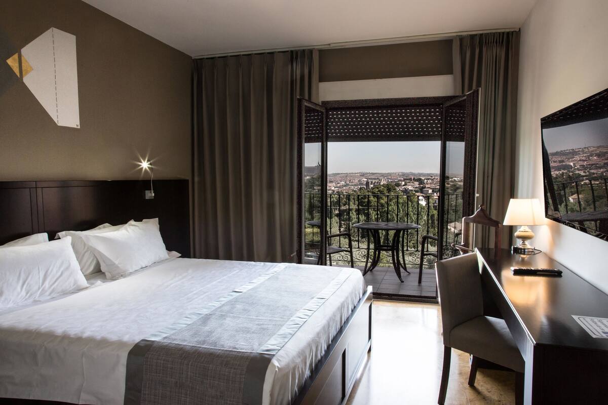 A hotel room with a large bed, a desk, and a balcony with a table and chairs.