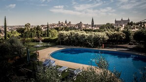 Piscina con sillas de descanso, rodeada de vegetación y con vistas a un paisaje urbano que incluye edificios históricos.
