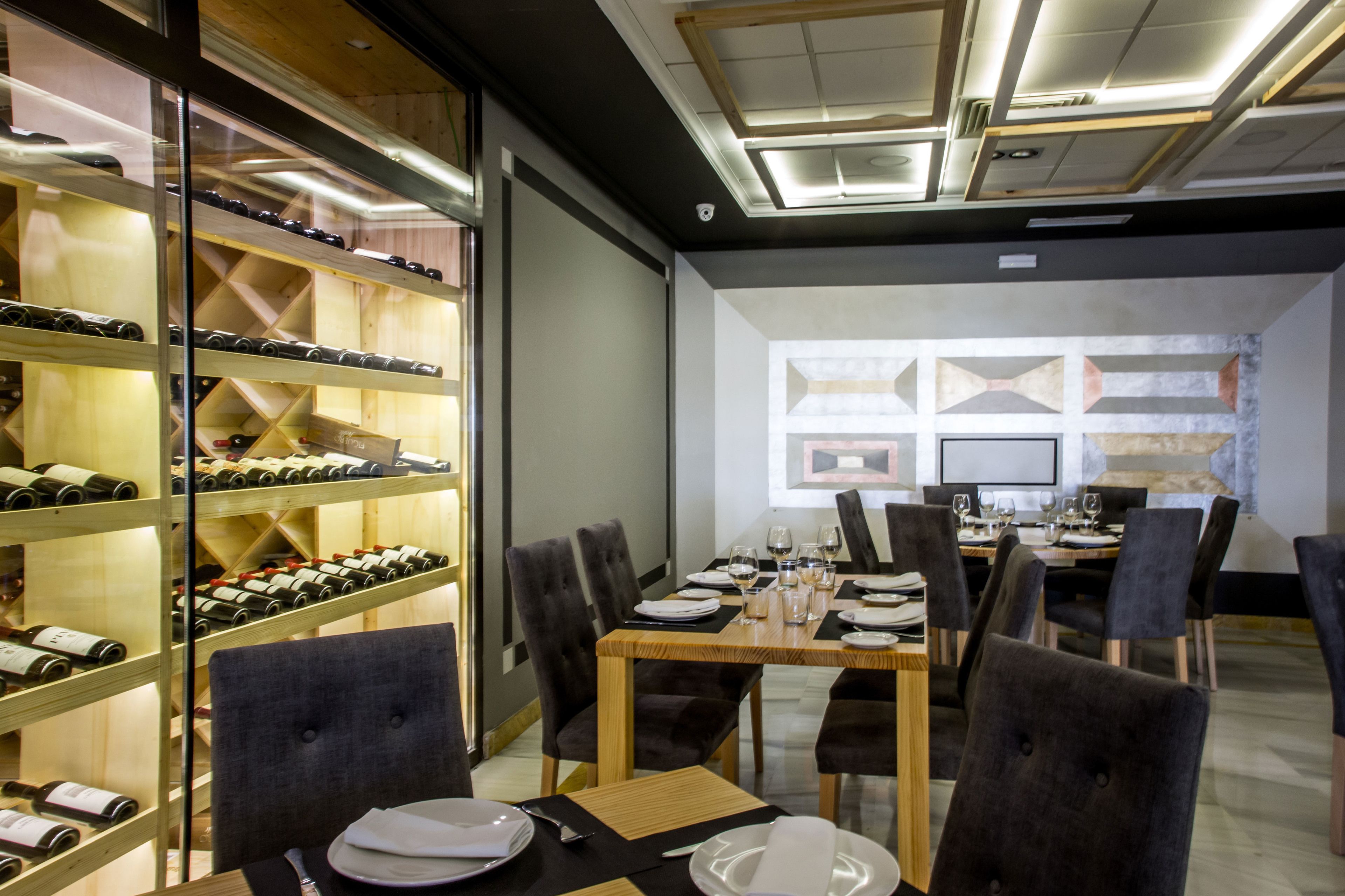 Un comedor con una mesa larga dispuesta para seis comensales, rodeada de sillas, y una estantería con botellas de vino a la izquierda.