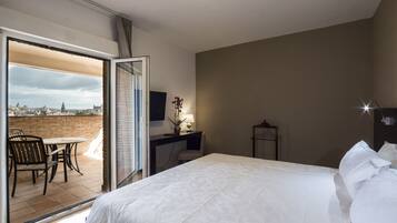 A hotel room with a bed, a desk, a chair, and a view of a cityscape through a glass door.