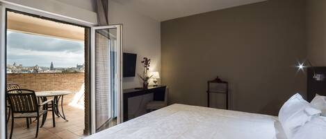 A hotel room with a bed, a desk, a chair, and a view of a cityscape through a glass door.