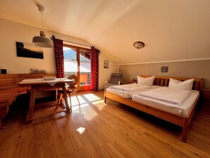 Une pièce avec un lit en bois, un bureau avec une chaise, une fenêtre avec des rideaux et un luminaire au plafond.