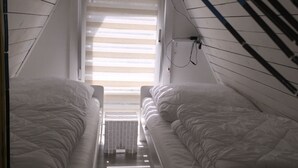 A narrow attic bedroom with two single beds, a sloped ceiling, and a window with blinds.