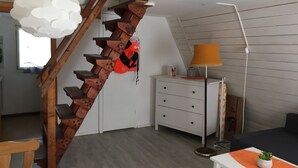 A modern interior with a wooden spiral staircase, a white dresser, a floor lamp, and a small table with a plant.