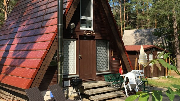 A small cabin with a sloped roof, a front door, and a window. There are outdoor seating areas with chairs and a table.