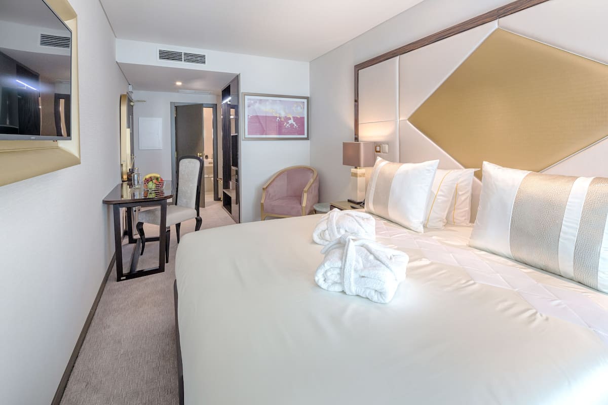 A hotel room with a large bed, a desk with a chair, a mirror, and a framed picture on the wall.