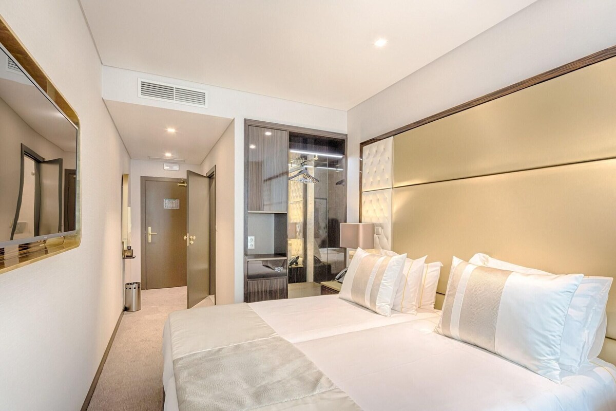 A hotel room with a large bed, a mirror, a wardrobe, and a bathroom visible through an open door.